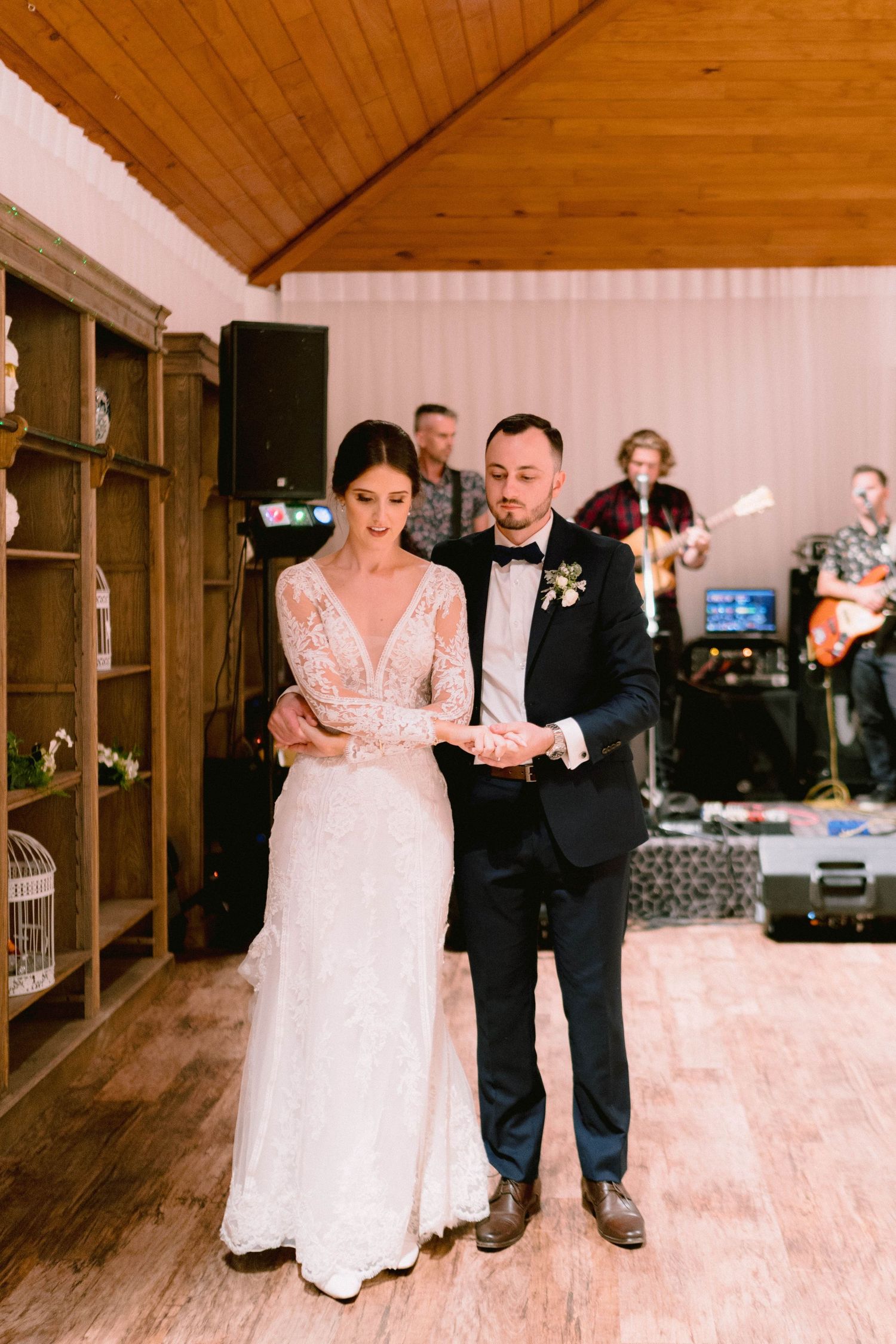 A couple shares their first dance in a rustic venue with wooden ceiling beams.