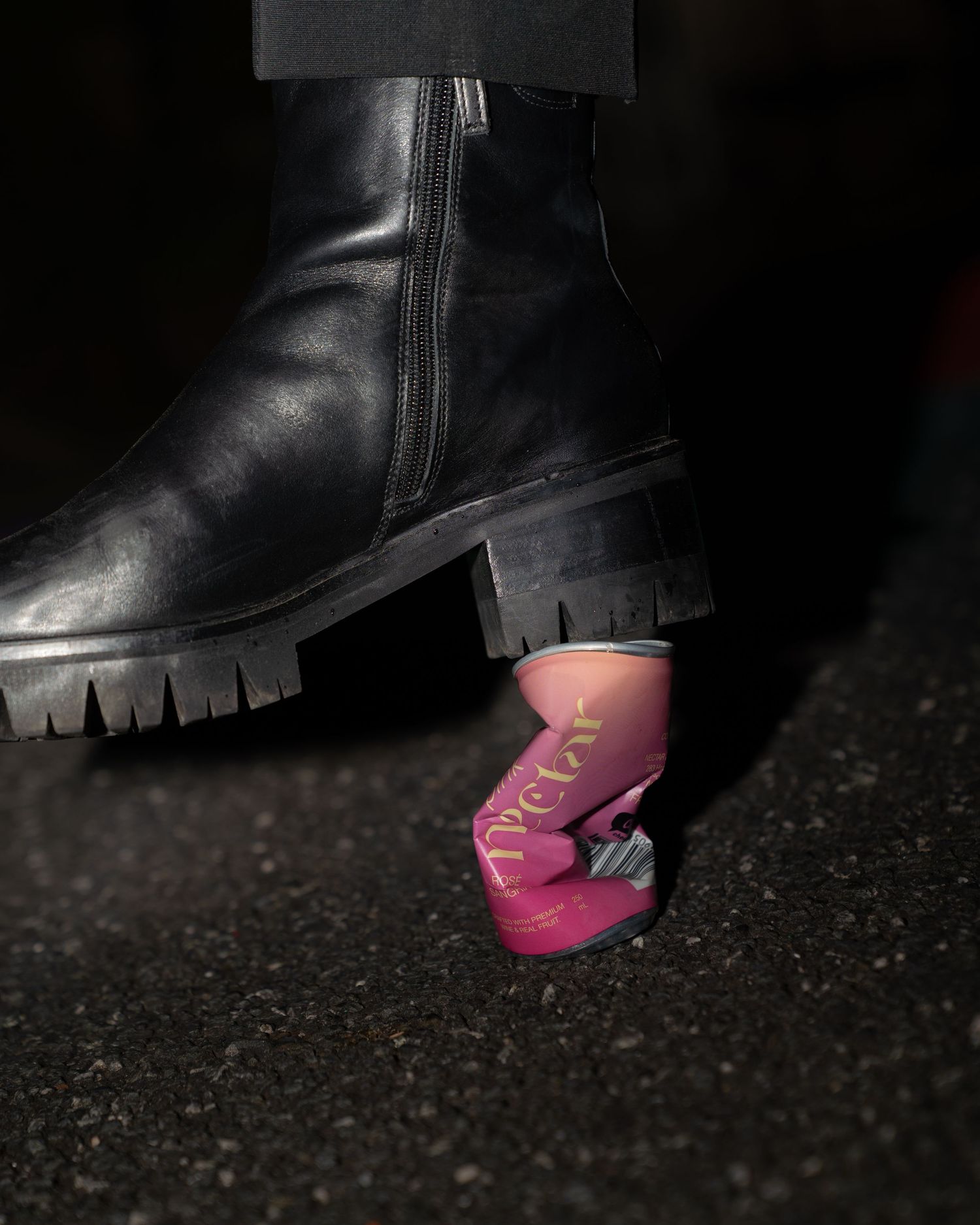 Black leather boot with bright pink sock visible at the ankle on dark textured ground.