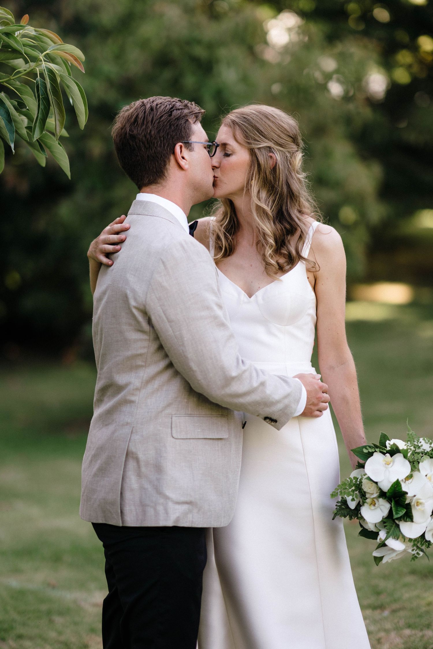 Romantic wedding couple shares intimate moment outdoors under green foliage.