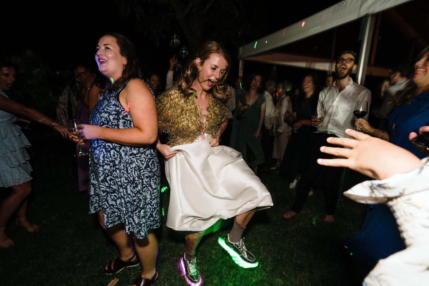 Wedding celebration on a dance floor at night with someone wearing tennis shoes under a formal dress.