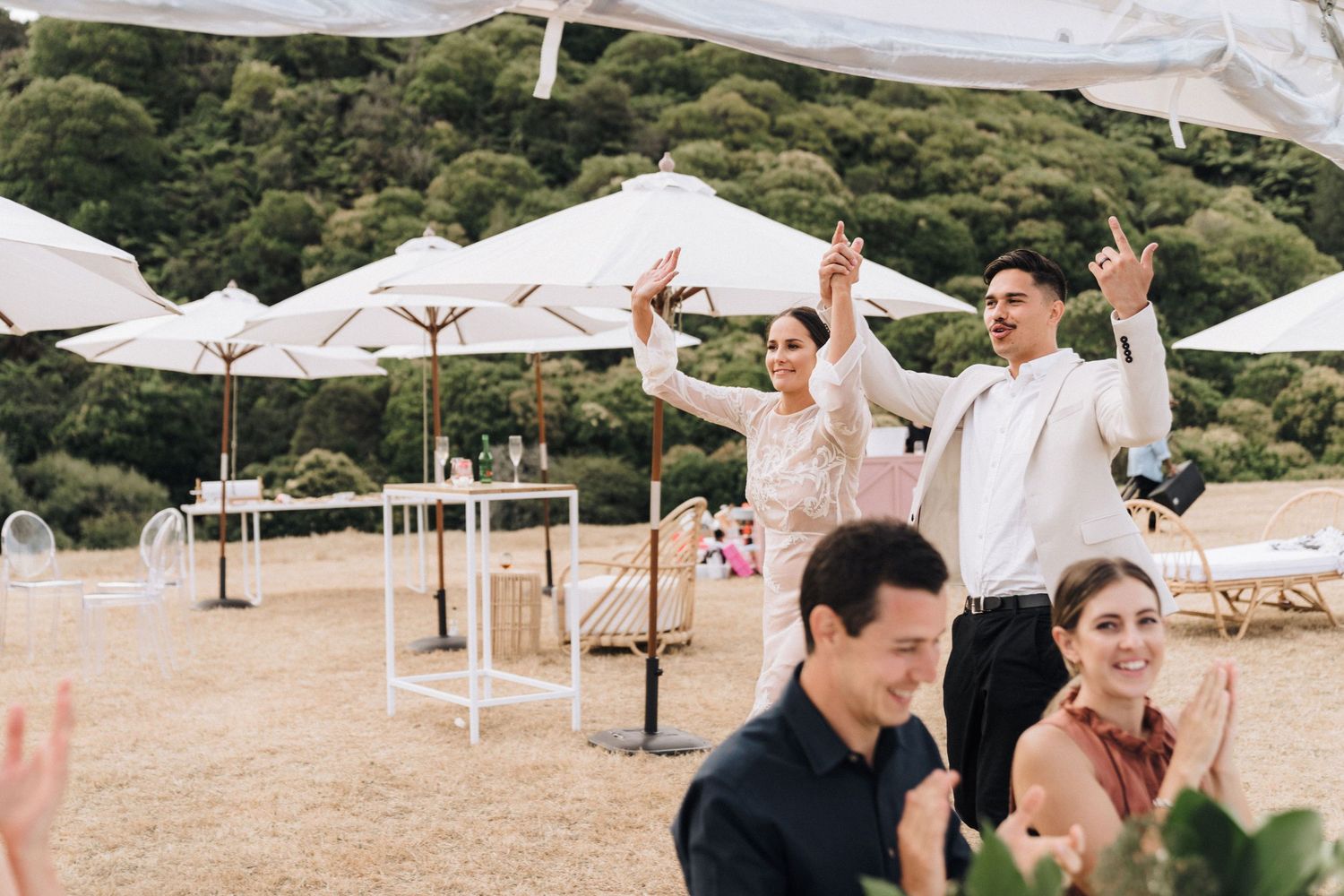 Outdoor event setup with white umbrellas and tables against a natural hillside backdrop.