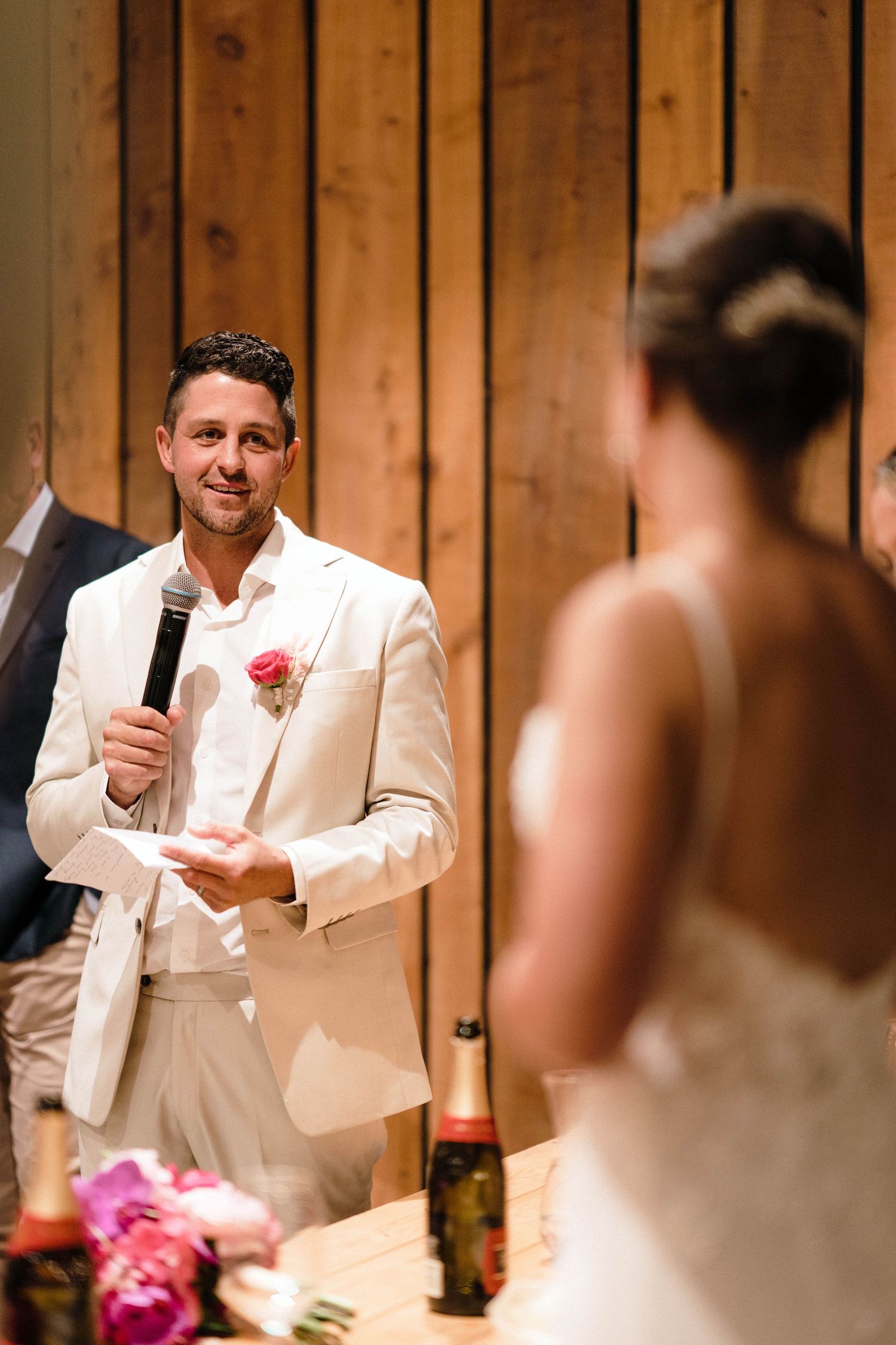 Wedding speeches being given in front of wooden paneled walls at a reception.