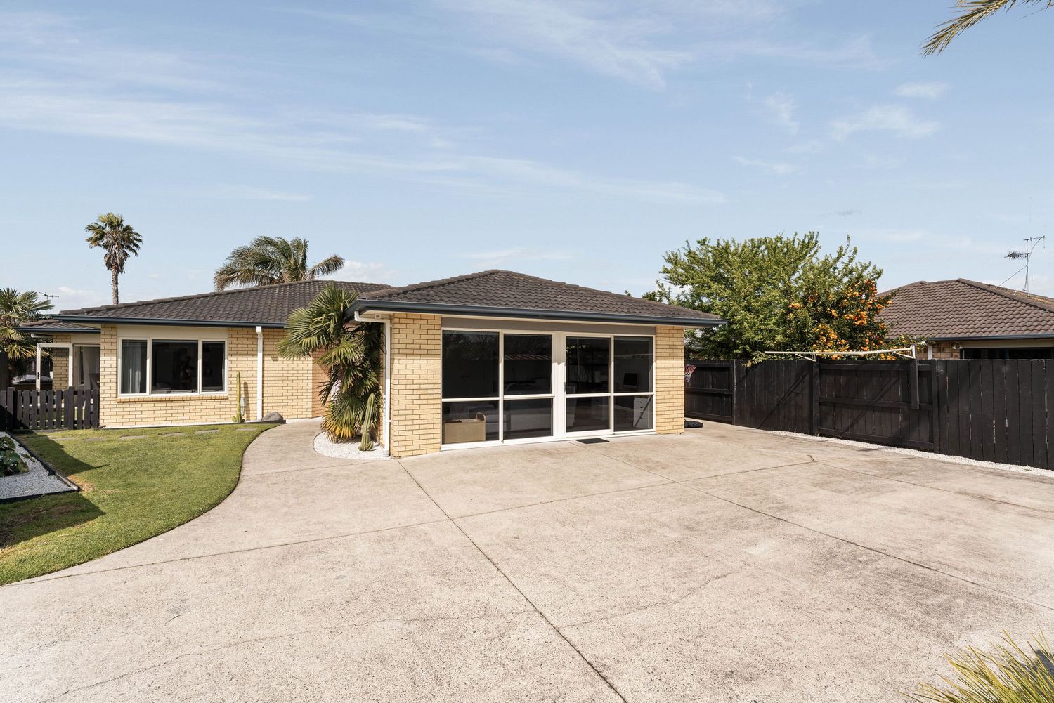 Single story beige home with screened lanai and large concrete driveway under blue sky with palm trees in Florida.