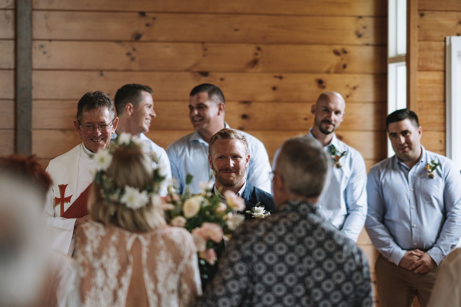 A small wedding ceremony takes place in a rustic wooden cabin with florals and casual attire.