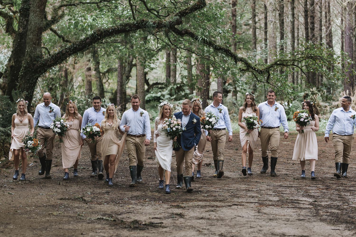 Group of wedding guests walk together on a wooded outdoor path wearing coordinated casual beige and white outfits.