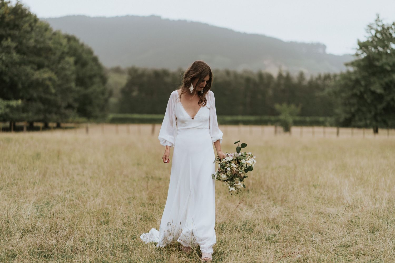 A dreamy scene of a flowing white dress in a golden meadow with misty mountains in the distance.