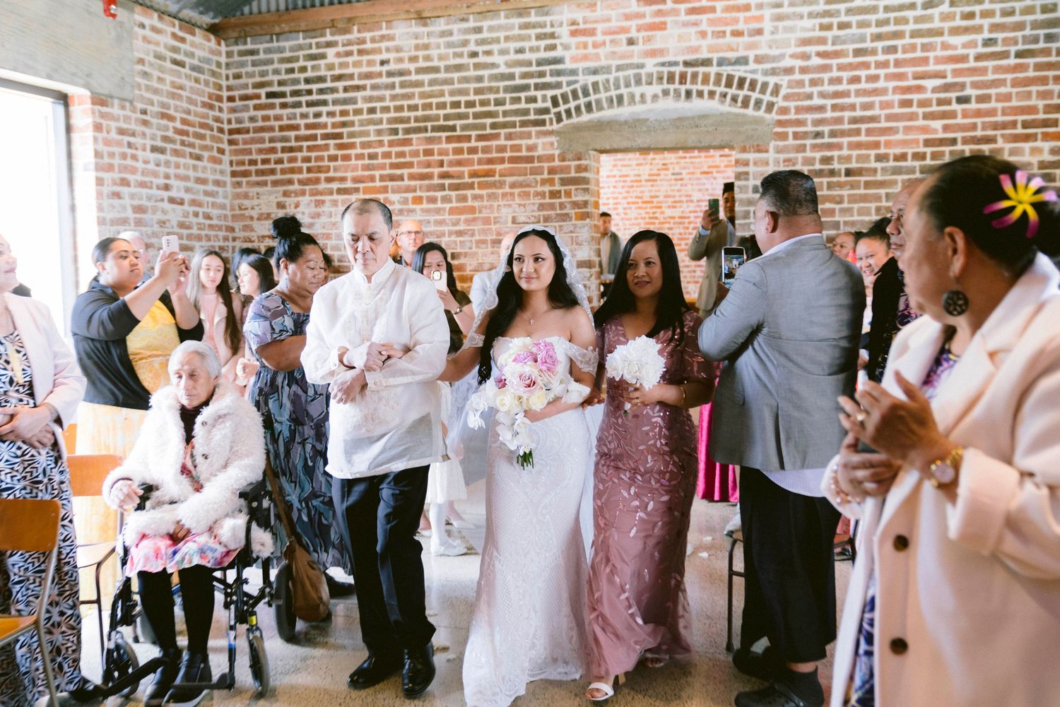 Wedding guests celebrate during a reception in a rustic brick-walled venue with elegant decor and floral arrangements.