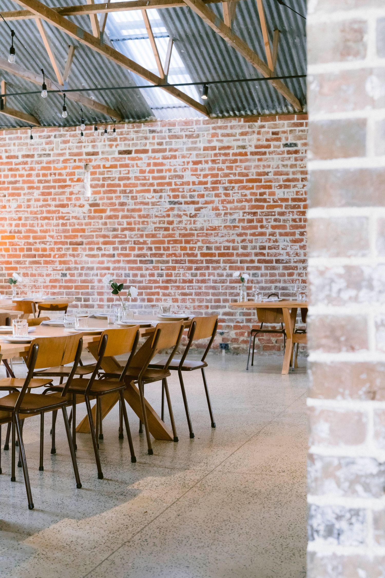Modern industrial wedding venue with exposed brick walls, wooden beams, and minimalist dining tables and chairs.