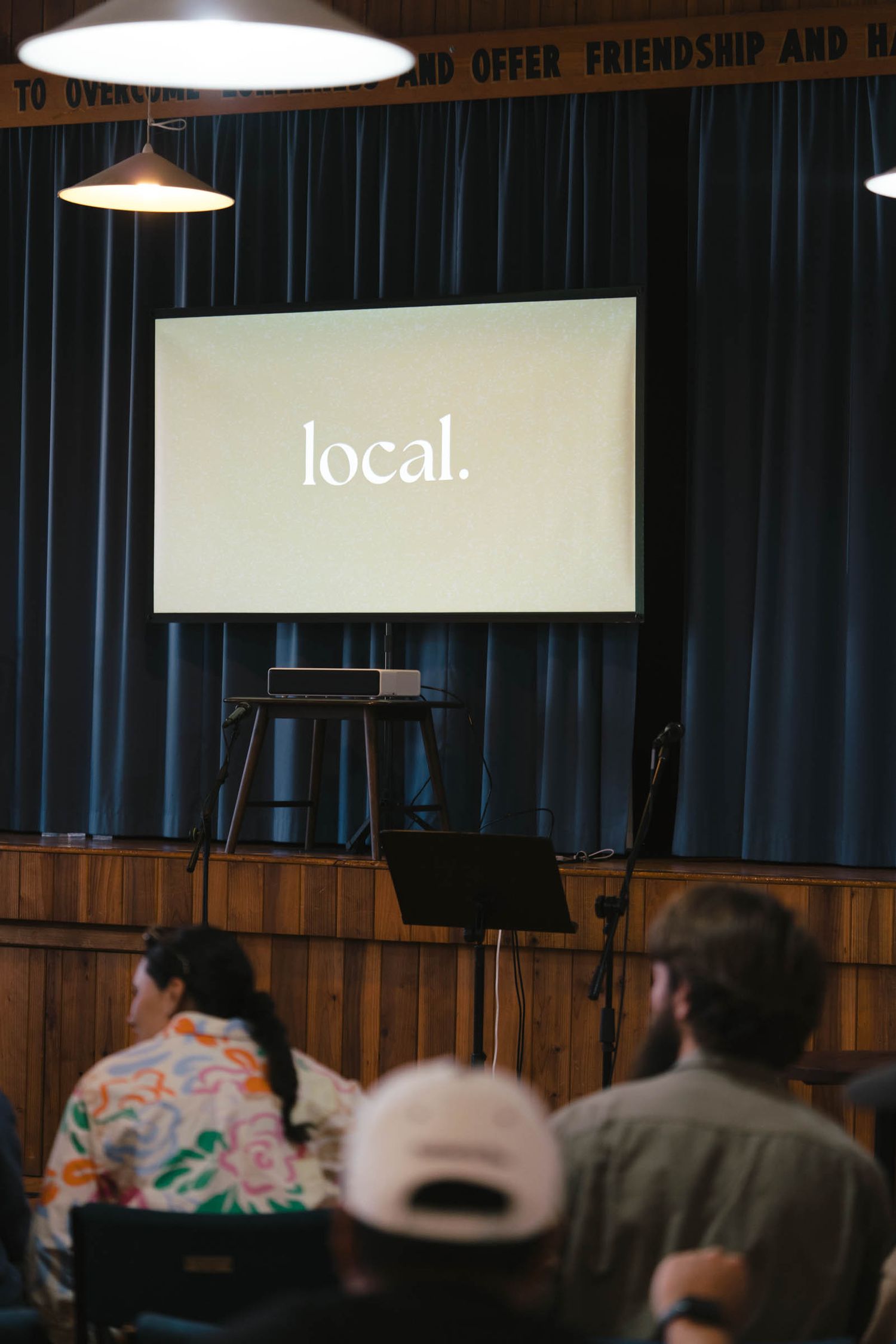 Interior of a meeting space with wood paneling, blue curtains and pendant lights displaying 'local' signage.