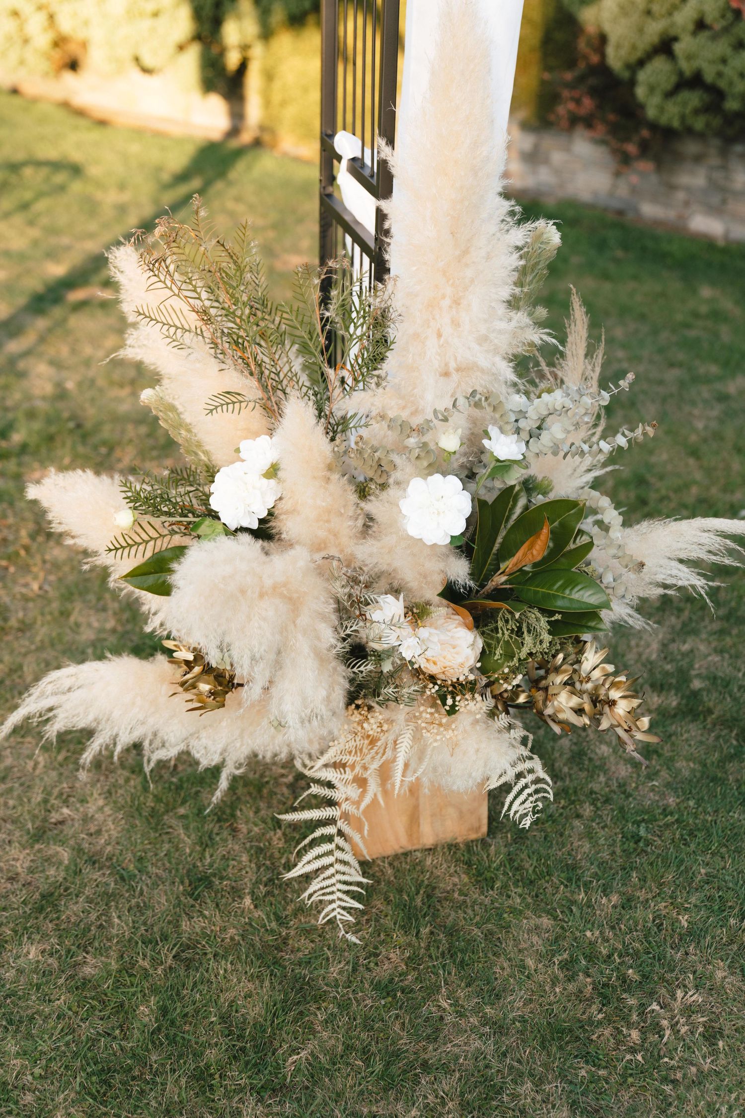 Elegant floral arrangement with pampas grass, white flowers and greenery in outdoor setting.
