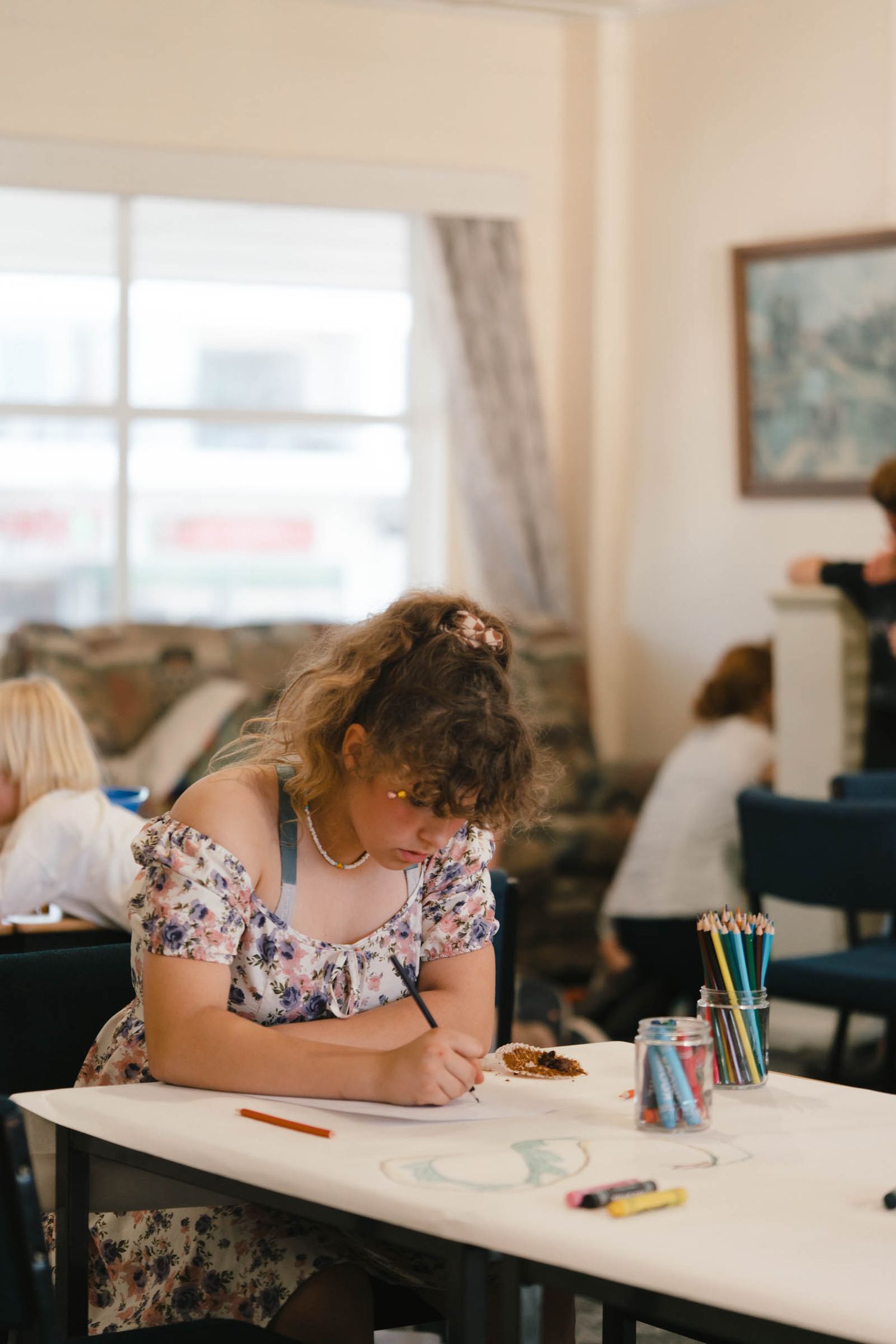 A person in a floral dress writing at a desk in a classroom setting.