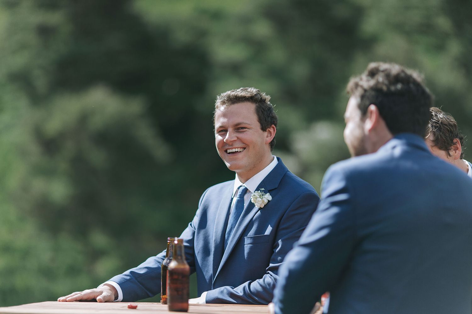 Two people in navy blue suits sharing a laugh during an outdoor celebration with beverages on table.