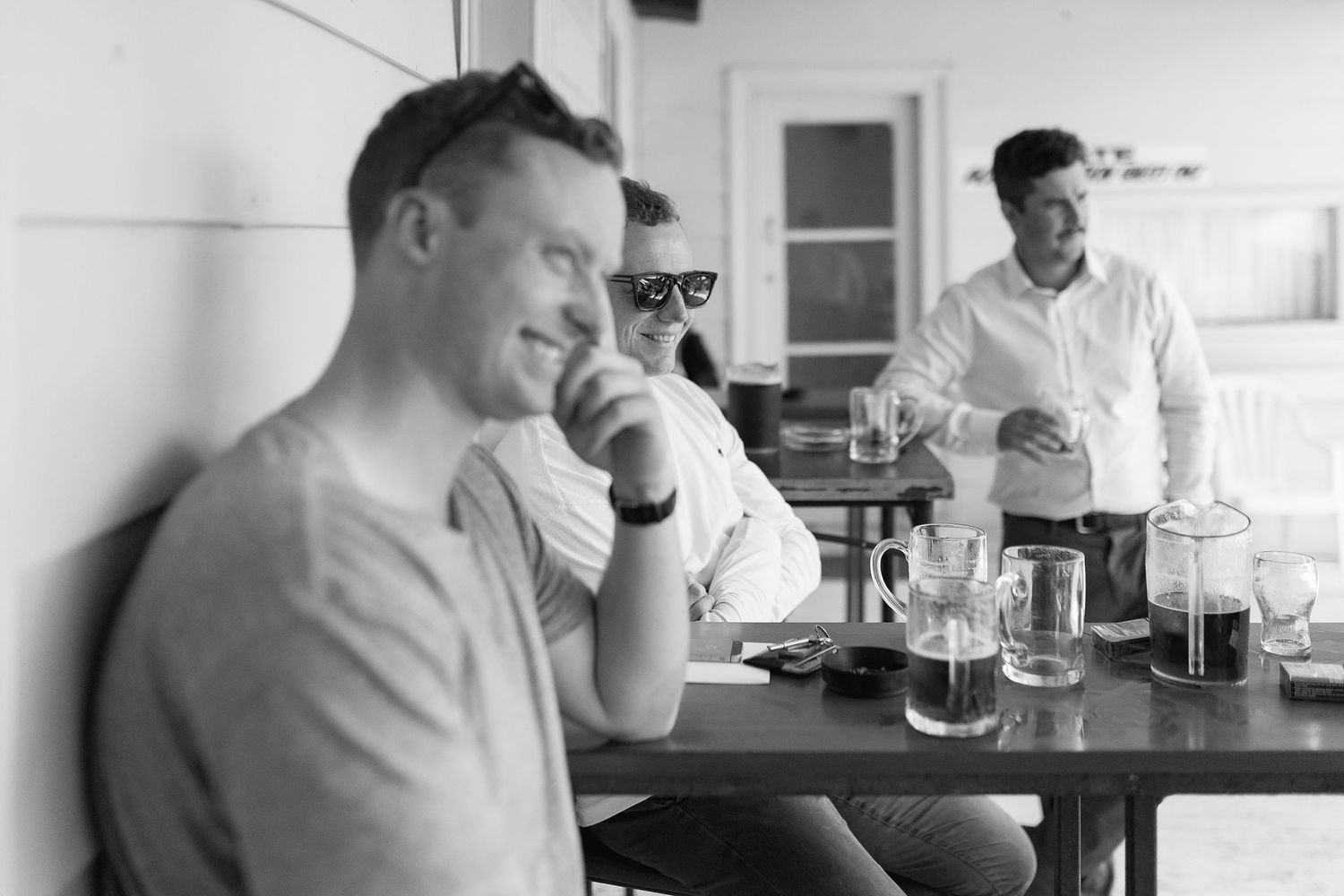 A black and white photo showing people relaxing at a cafe counter with glasses of drinks on the bar.