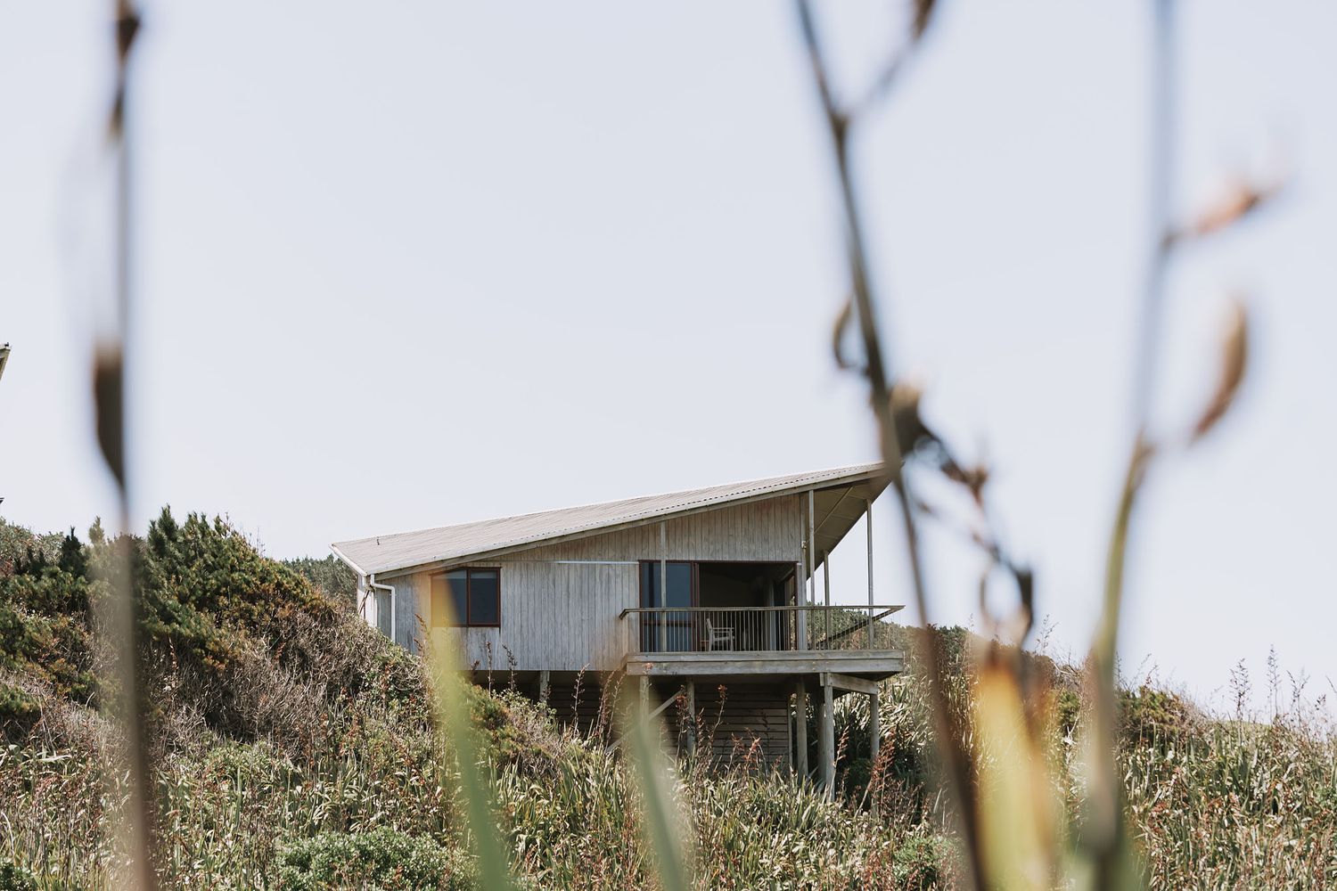 A modern minimalist house with an infinity pool sits perched above the ocean overlooking the coastal shoreline.