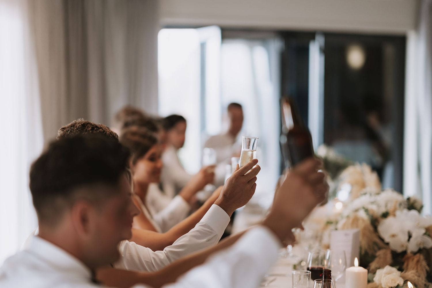 A group of people seated at an elegant wedding reception dinner table with white floral centerpieces.