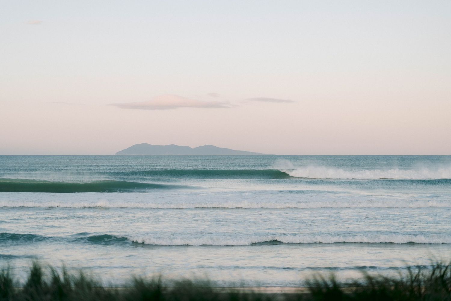 Serene ocean waves roll in under a pastel sky with distant mountains on the horizon.