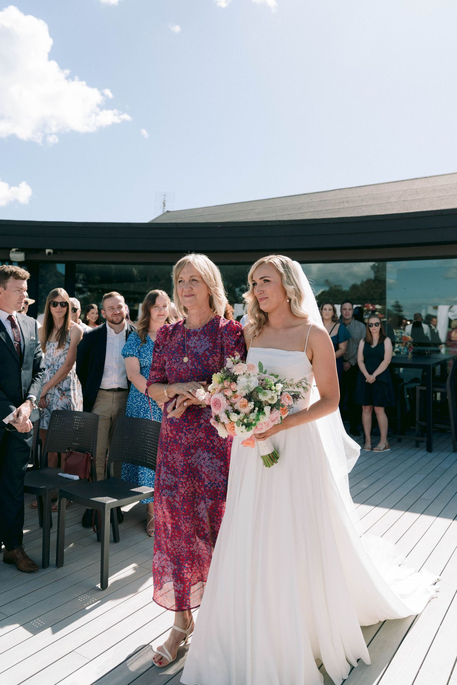 Wedding ceremony on a modern deck with guests seated and floral decorations.
