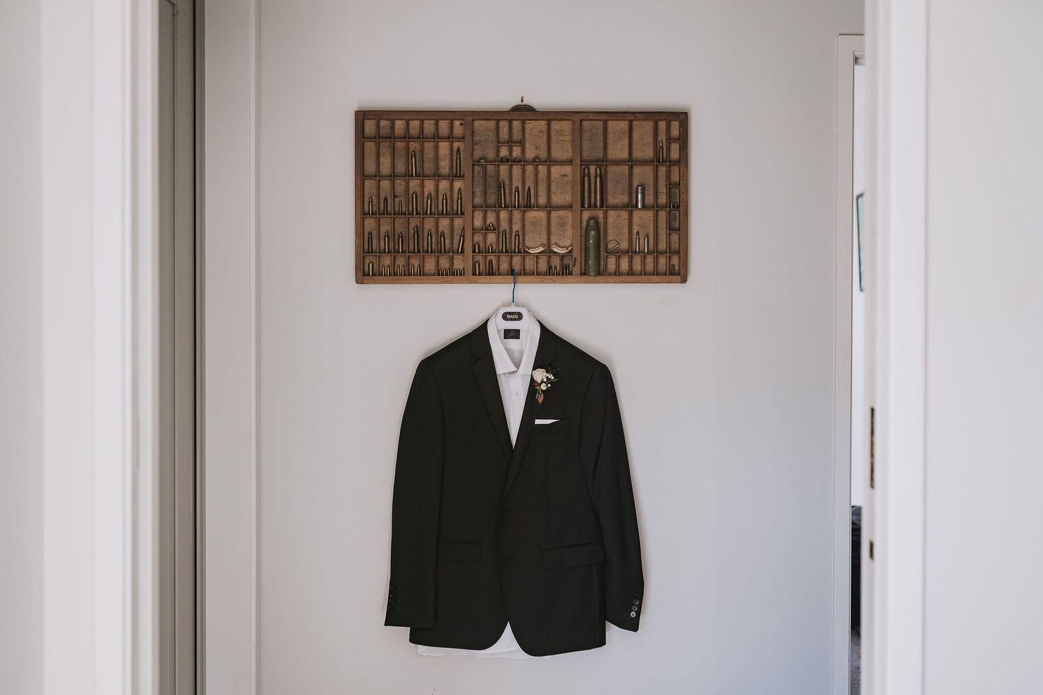 Three black formal suit jackets hang neatly on white hangers against a minimalist white wall.