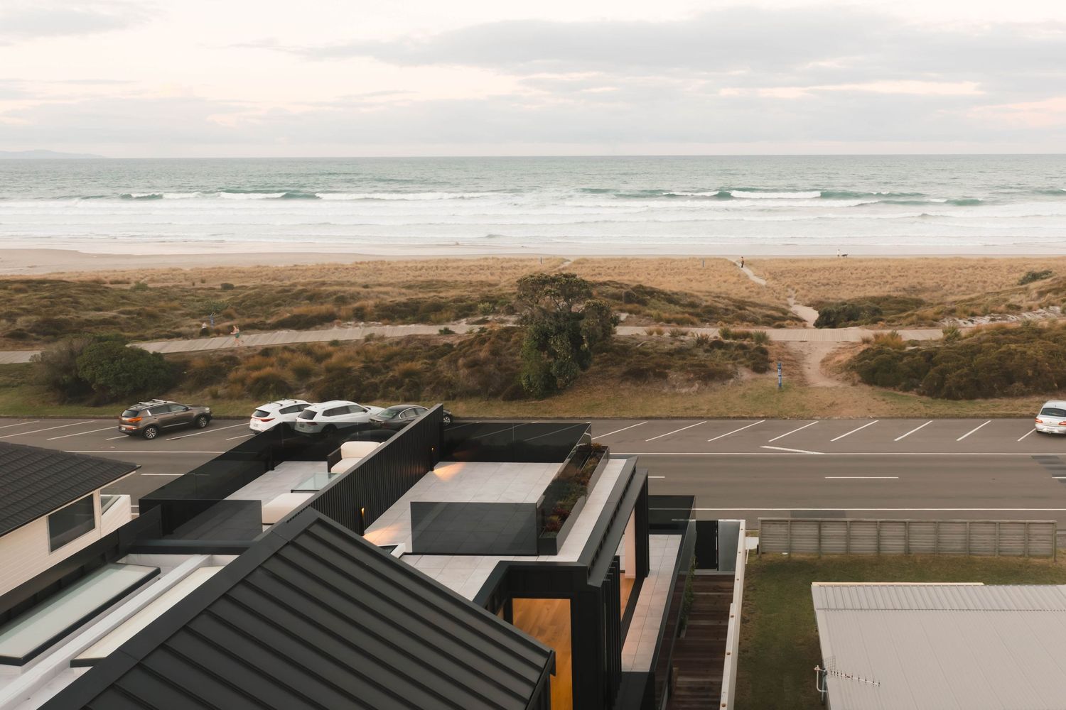 A scenic coastal landscape with sandy beaches, ocean waves, and natural dunes stretching along the shoreline at sunset.