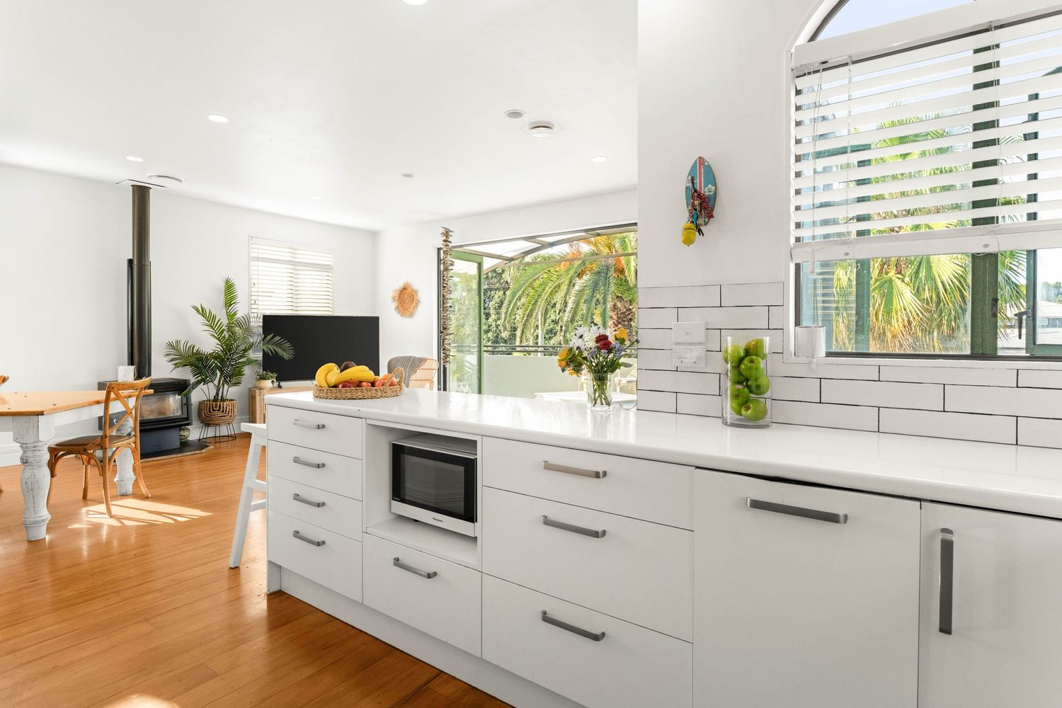 Contemporary white kitchen with long countertops, wooden floors and natural light from windows.
