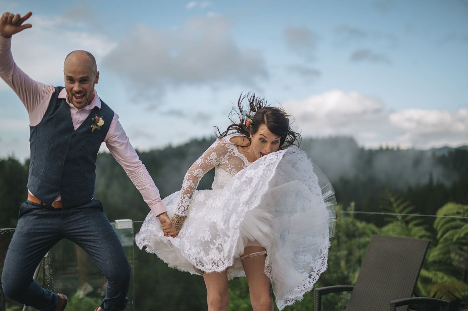 A joyful couple dances together outdoors in front of scenic mountain views as her lace dress flows in the breeze.