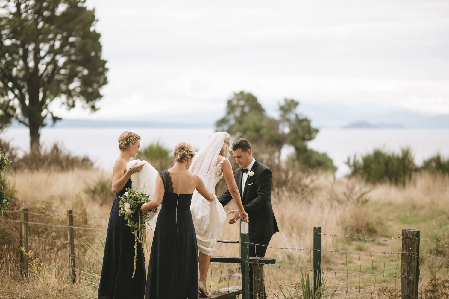 Wedding party walks along a rustic fence line in an outdoor setting with ocean views.