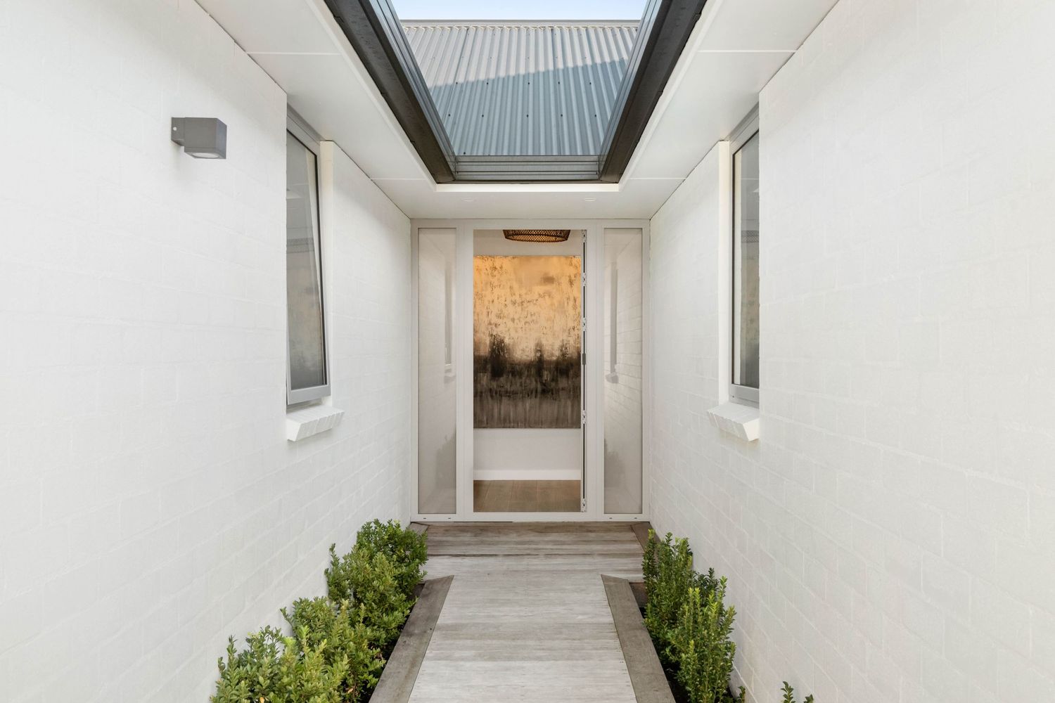 Bright white hallway with skylights and potted plants along the walls.