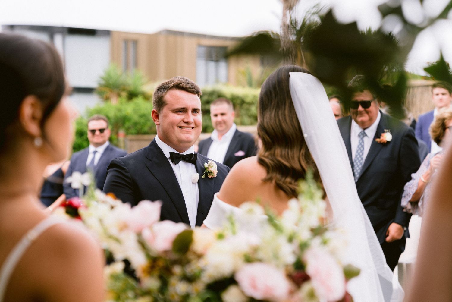 Wedding ceremony guests gathered outdoors surrounded by soft pink floral decorations.