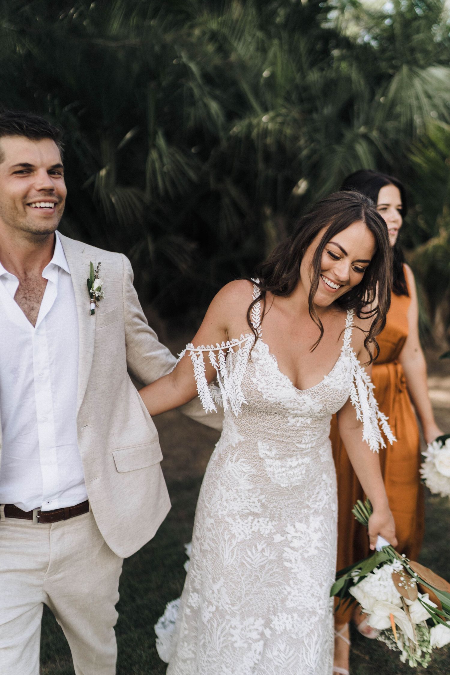Romantic wedding couple in white attire sharing intimate moments among palm trees during an outdoor photoshoot.