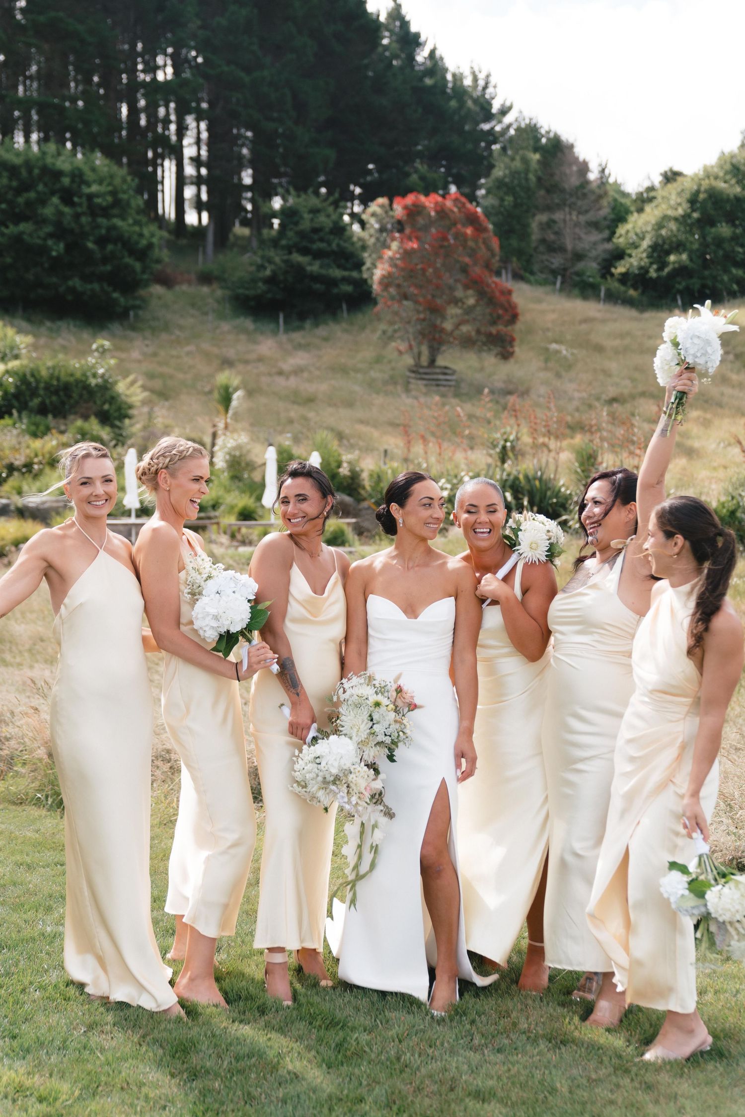 Bridesmaids in cream-colored dresses posing together on a hillside.