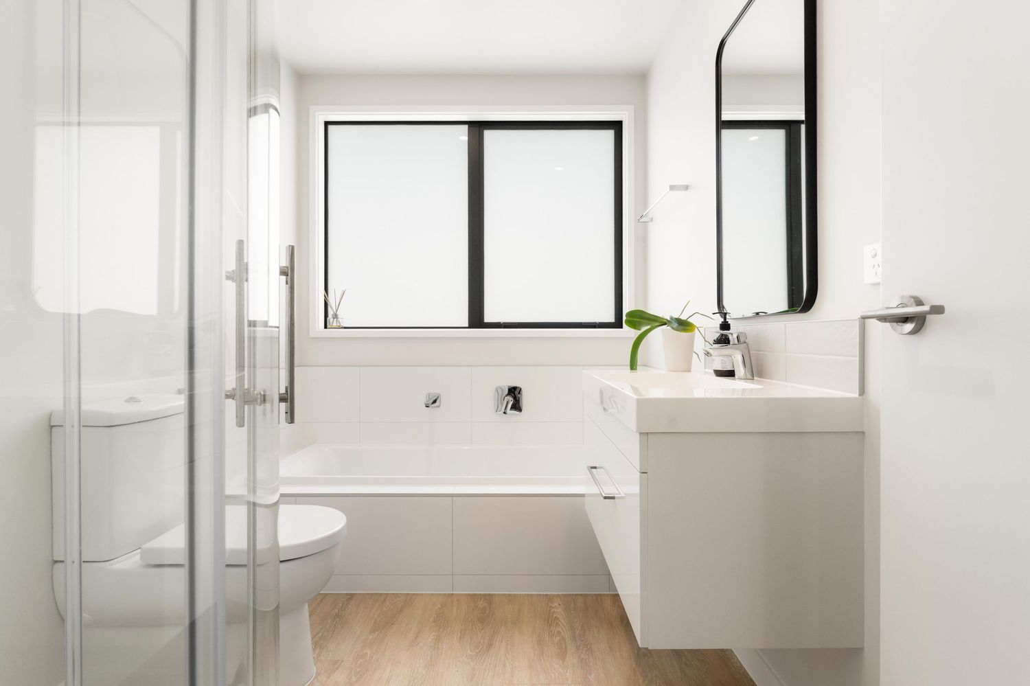 Bright white bathroom with modern fixtures, black-framed windows, and clean lines.