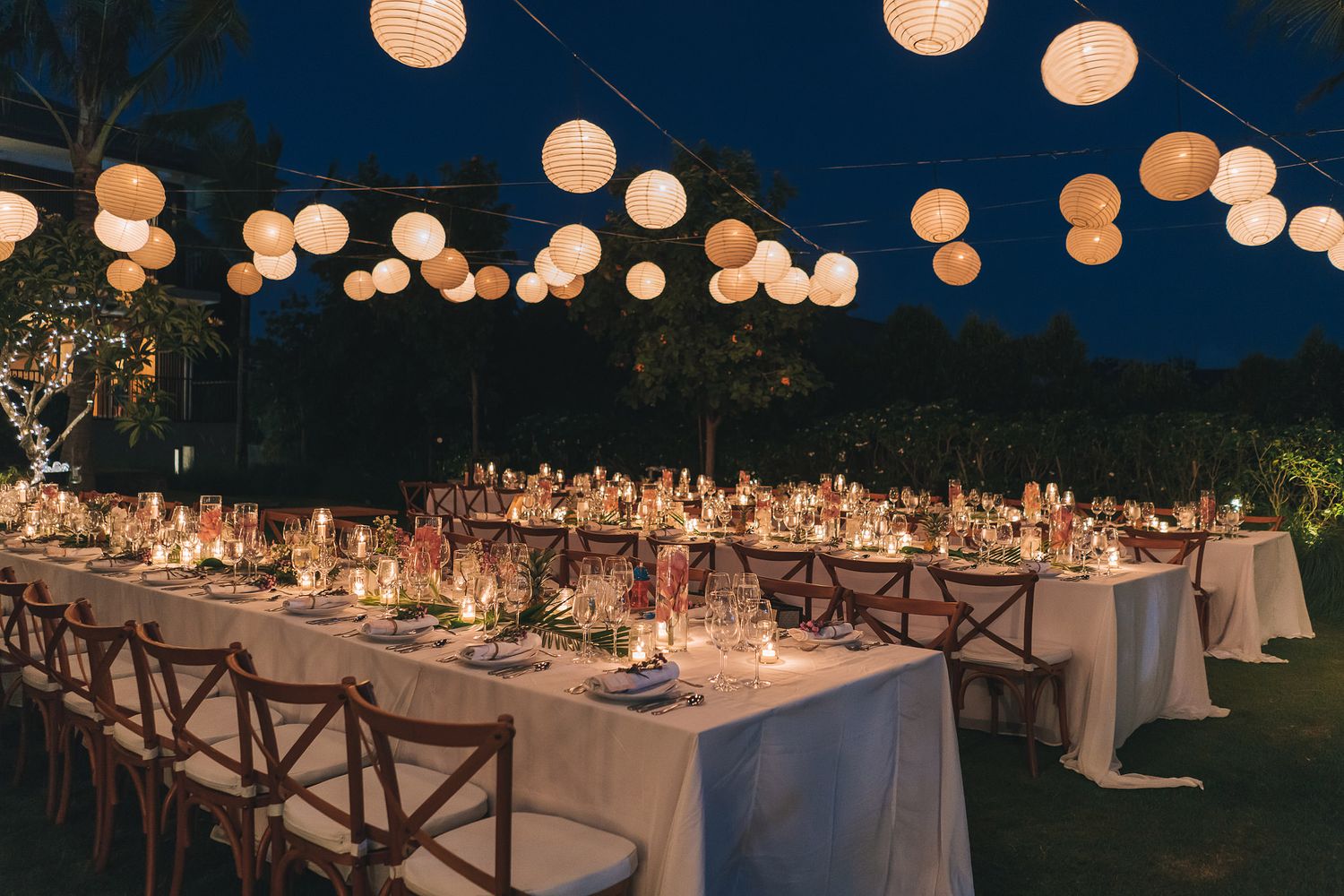 Evening wedding reception tables under glowing paper lanterns on a lawn.