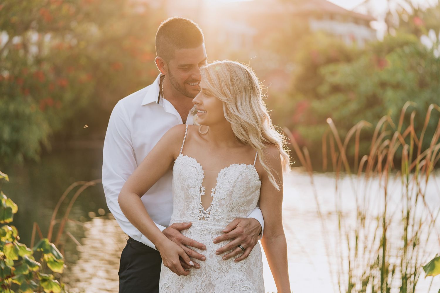 Romantic newlywed couple embraces by a tranquil lake during golden hour sunset photography session.