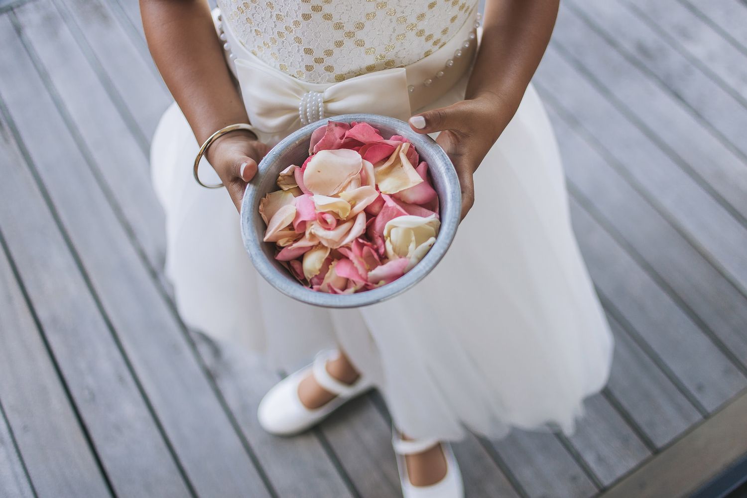 White-dressed attendants holding baskets of pink rose petals at outdoor celebration.