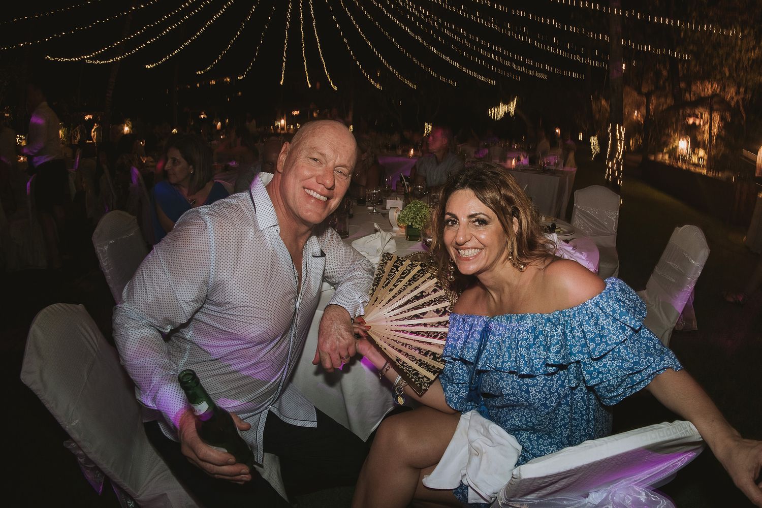 Wedding guests enjoying festive celebration with decorative hand fan at night reception.