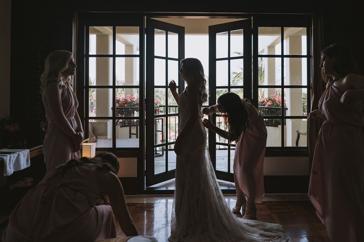 Silhouettes of people helping with a wedding dress preparation against French doors.