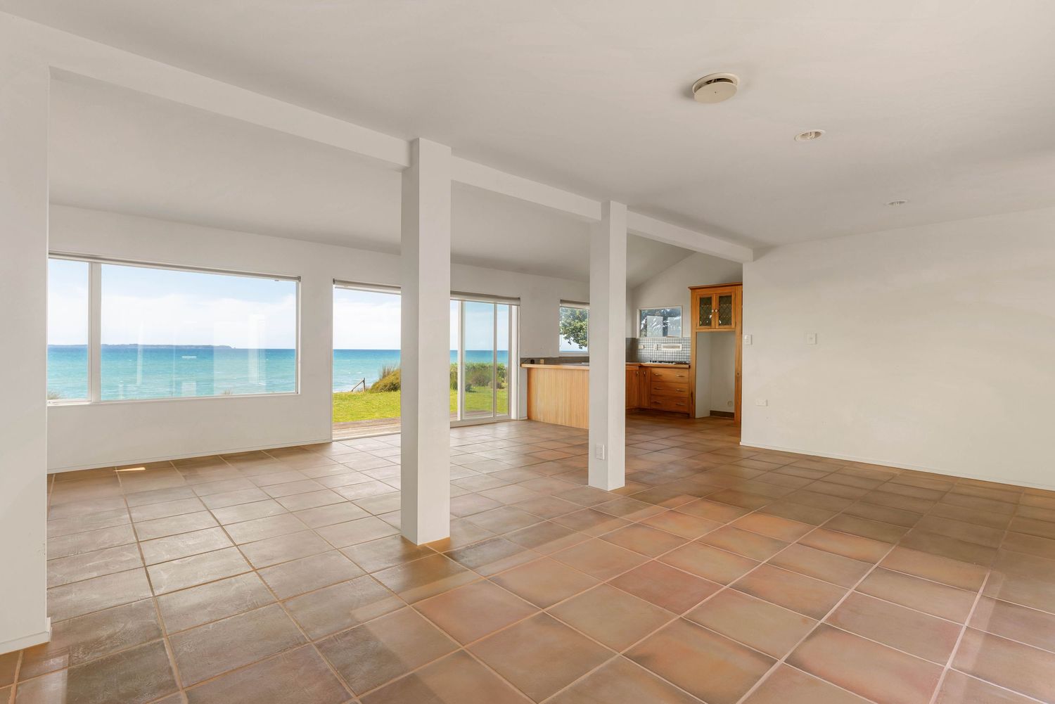 Spacious open-concept living area with terracotta tile floors and expansive ocean views through large windows.