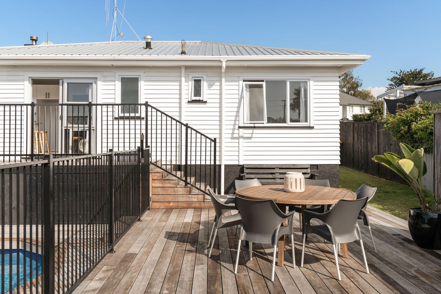 White house exterior with wooden deck featuring outdoor dining set and pool fence.