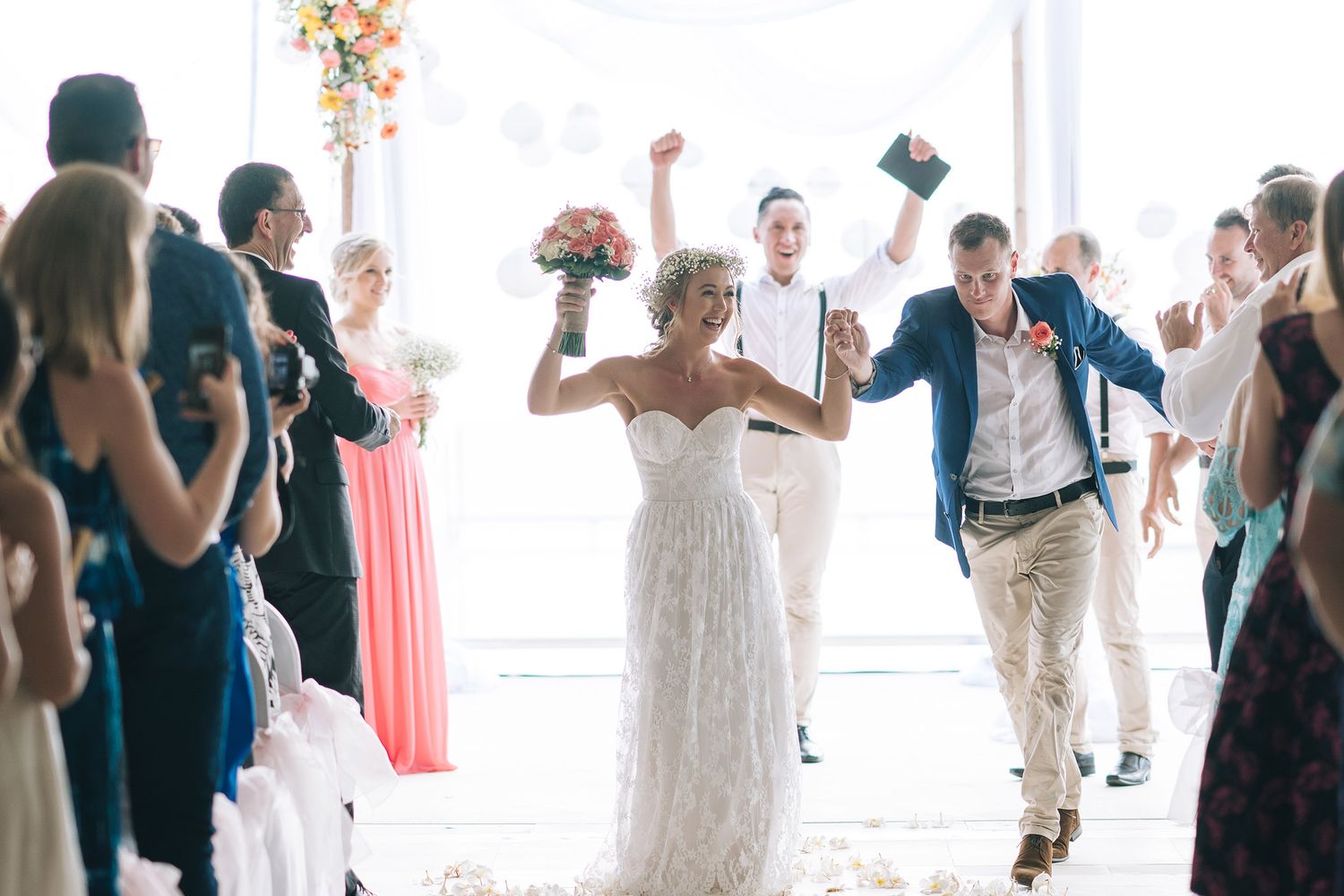 Joyful wedding couple celebrates while exiting their ceremony surrounded by guests.