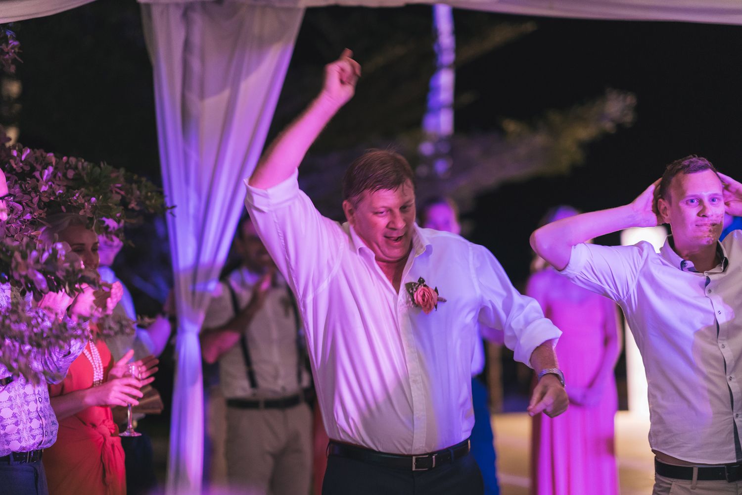 Wedding party dancing and celebrating under purple mood lighting at an evening reception.