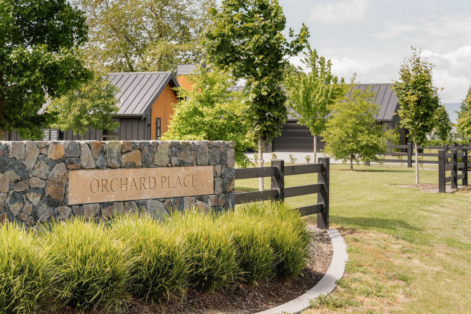 Rustic stone entrance wall with 'Orchard House' sign and wooden fence surrounded by landscaping.