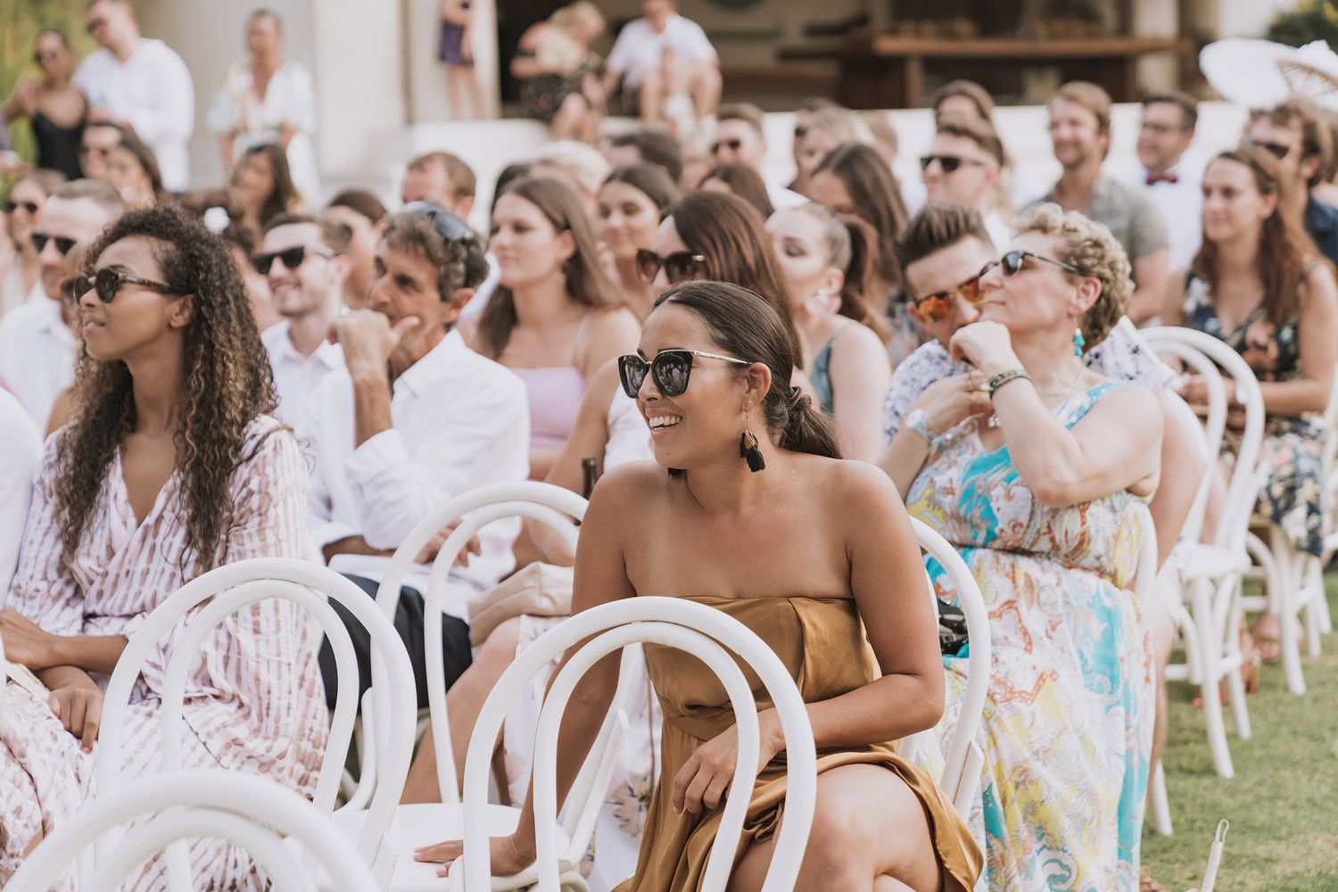Wedding guests dressed in white seated outdoors at a casual garden reception.