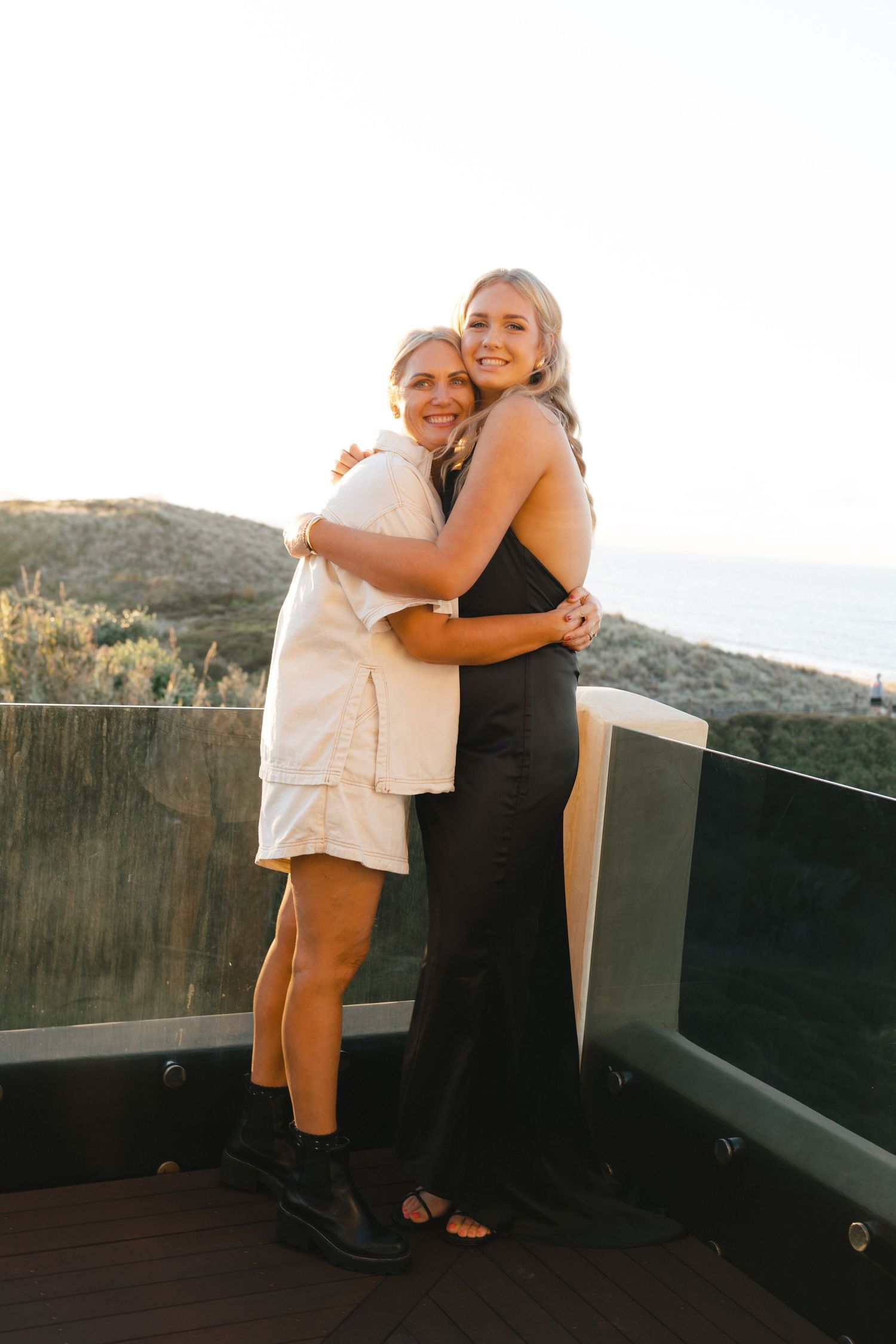 Friends embracing and laughing together on outdoor deck with scenic mountain backdrop.