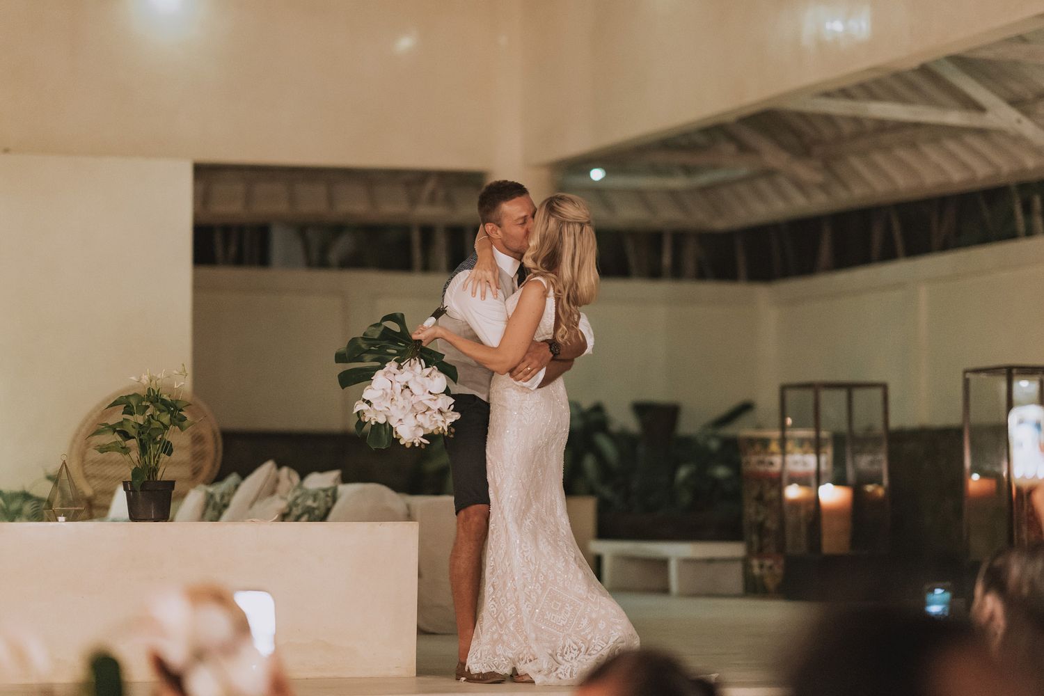 Couple dancing in elegant indoor venue with tropical plants and modern decor.