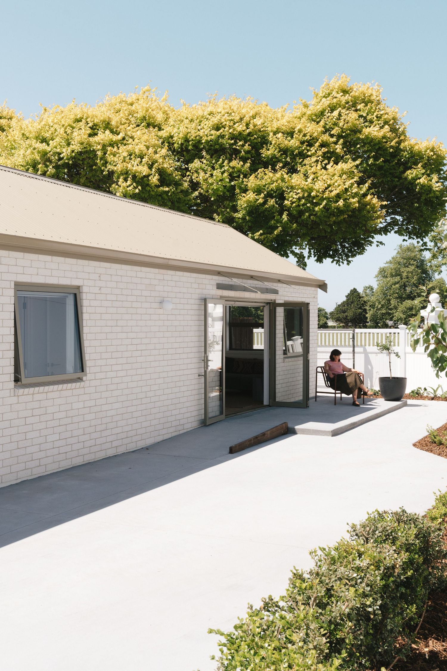 Modern white brick building exterior with curved walls and landscaping under blue sky.