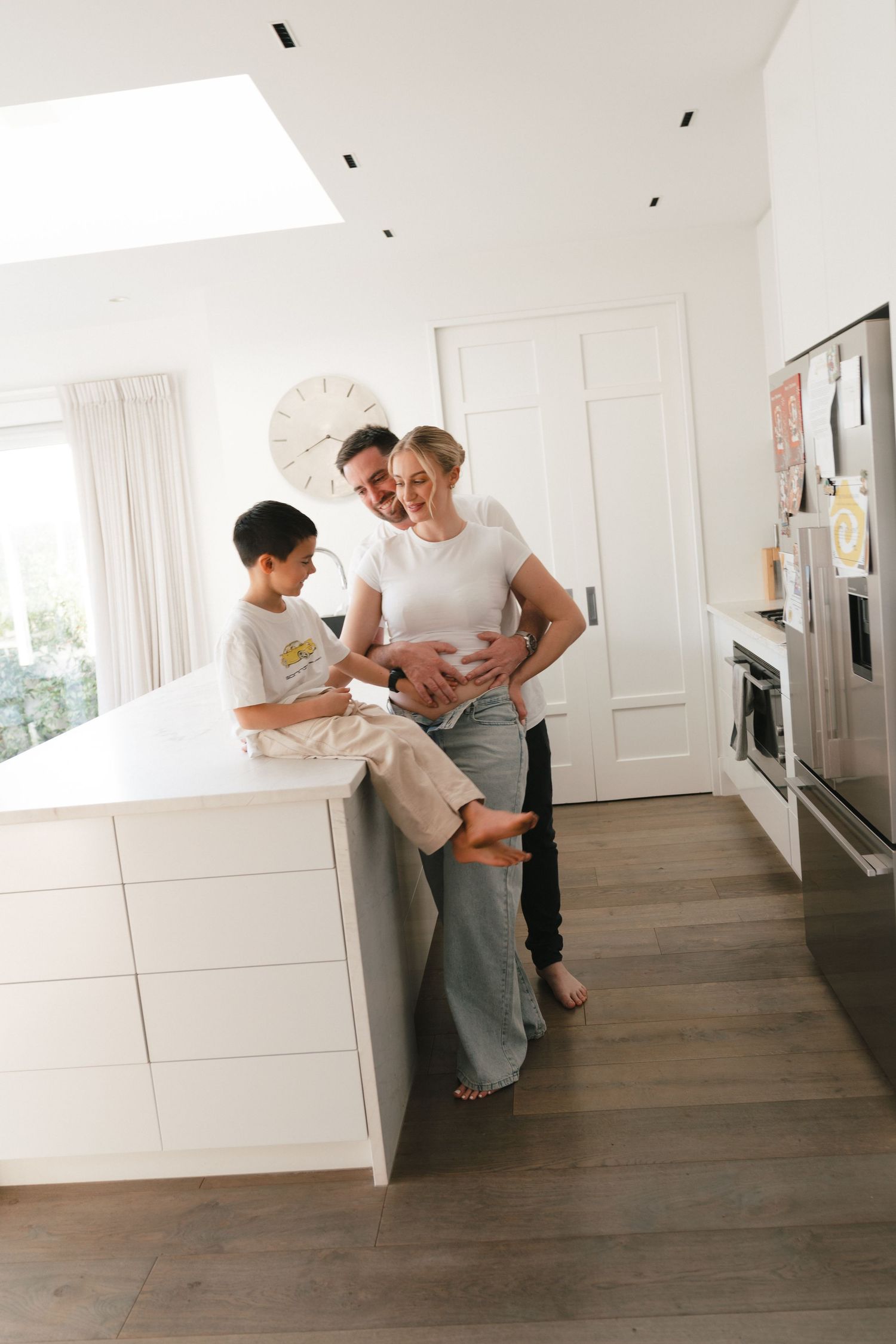 Relaxed family moment in modern white kitchen with hardwood floors, sharing smiles and togetherness.