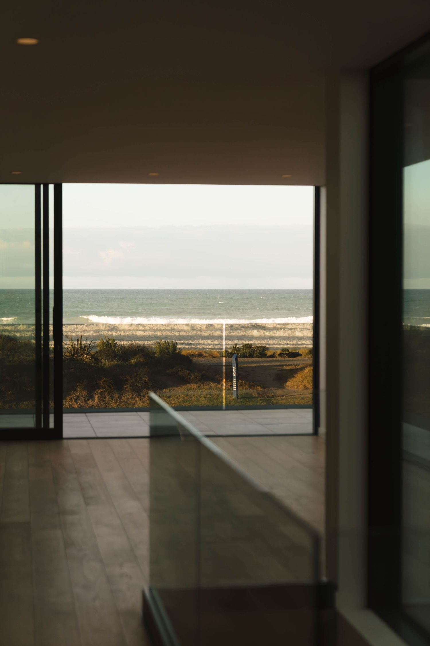 Modern coastal home interior with floor-to-ceiling windows offering a scenic ocean view through glass balcony railings.
