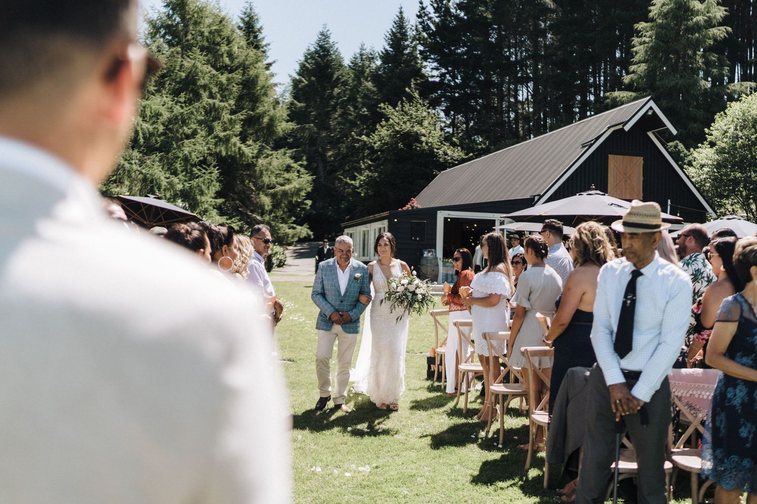 Guests gathered at an outdoor wedding ceremony with a rustic cabin and evergreen trees in the background.