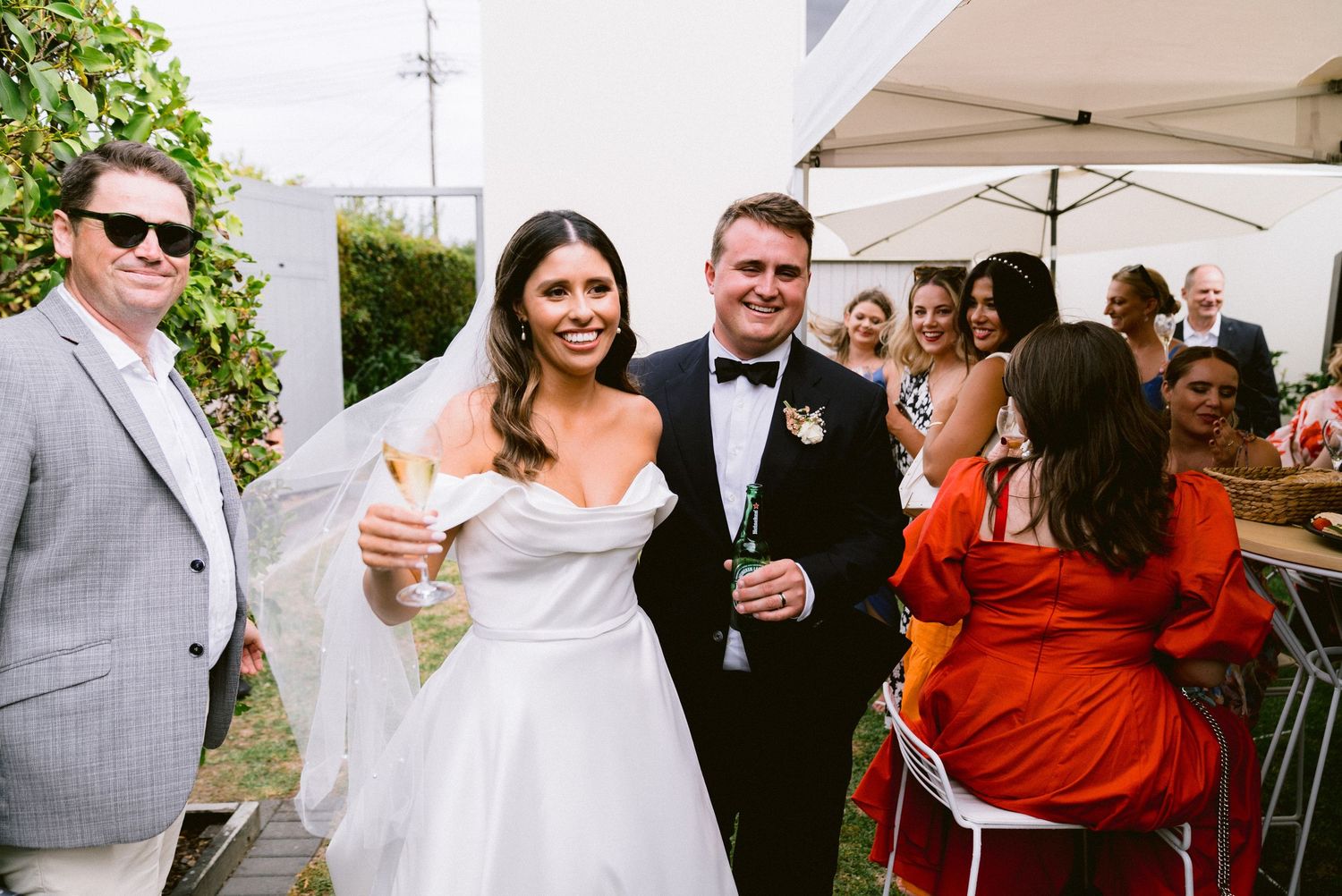 Wedding guests celebrating with drinks under an outdoor tent during the reception.