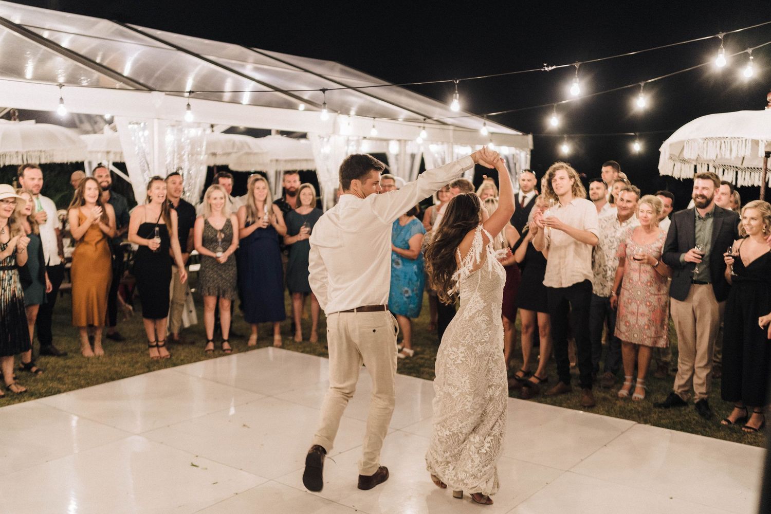 Couple dances on an outdoor dance floor while wedding guests cheer and watch from the sides.